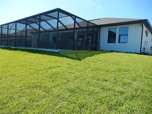Back of property with a lawn, glass enclosure, stucco siding, a sunroom, and roof with shingles