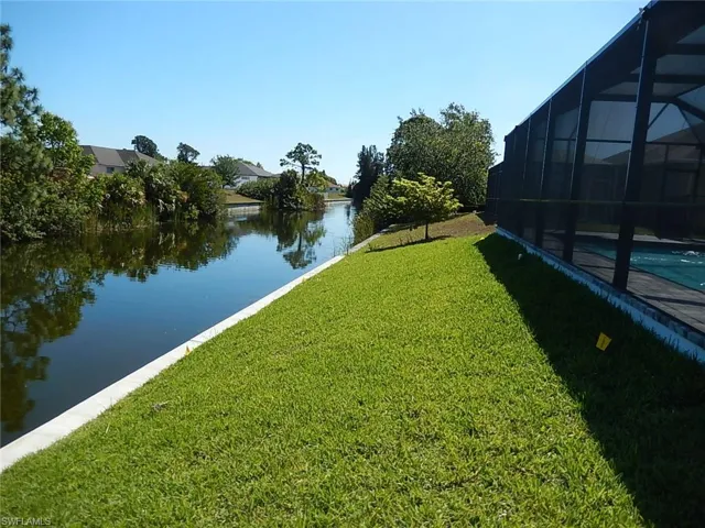 View of grassy yard featuring an outdoor pool, a sunroom, glass enclosure, and a water view