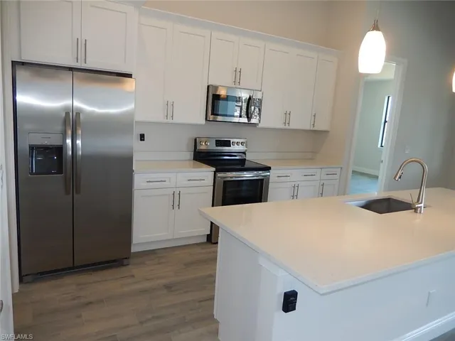 Kitchen with appliances with stainless steel finishes, white cabinetry, light stone countertops, dark wood-style floors, and pendant lighting