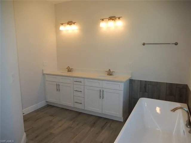 Full bath featuring double vanity, a soaking tub, and dark wood-type flooring