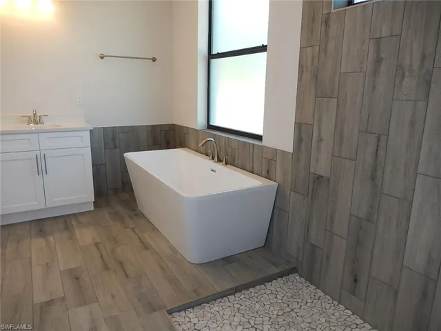 Bathroom with vanity, a freestanding bath, tile walls, light wood finished floors, and wainscoting