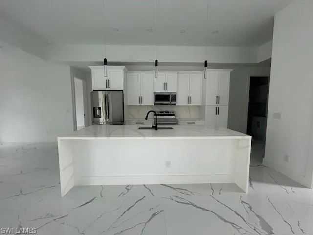 Kitchen with light stone counters, stainless steel appliances, white cabinetry, and a large island with sink