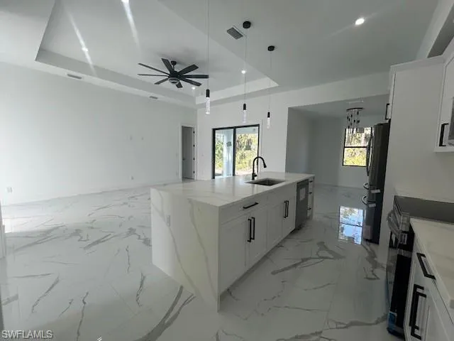 Kitchen featuring white cabinets, light stone counters, open floor plan, a raised ceiling, and decorative light fixtures