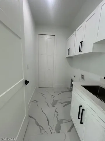 Washroom with cabinet space, hookup for a washing machine, light marble finish flooring, and hookup for an electric dryer