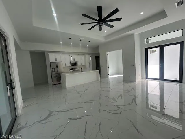 Unfurnished living room featuring a raised ceiling, light marble finish floors, a ceiling fan, and recessed lighting
