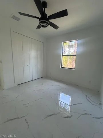 Unfurnished bedroom featuring light marble finish floors, a ceiling fan, and a closet
