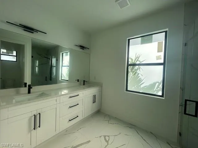 Full bathroom with a marble finish shower, double vanity, and light marble finish flooring