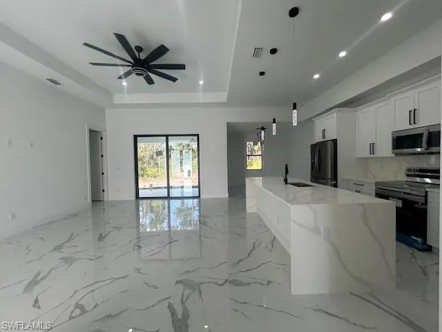 Kitchen featuring stainless steel appliances, pendant lighting, open floor plan, white cabinetry, and light marble finish floors