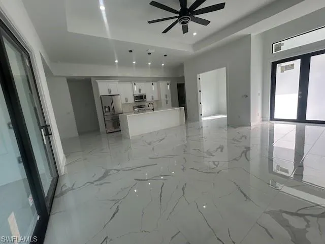 Unfurnished living room with a tray ceiling, light marble finish floors, recessed lighting, and a ceiling fan
