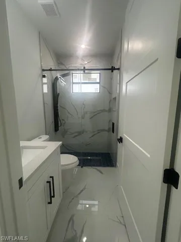 Full bathroom featuring light marble finish flooring, vanity, and a marble finish shower