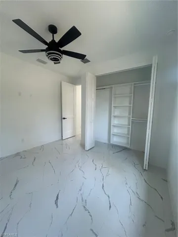 Unfurnished bedroom featuring light marble finish flooring, a ceiling fan, and a closet