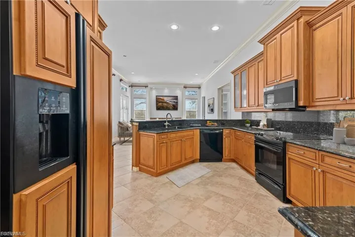 Kitchen featuring ornamental molding, a peninsula, wood finish cabinets, black appliances, and dark stone countertops