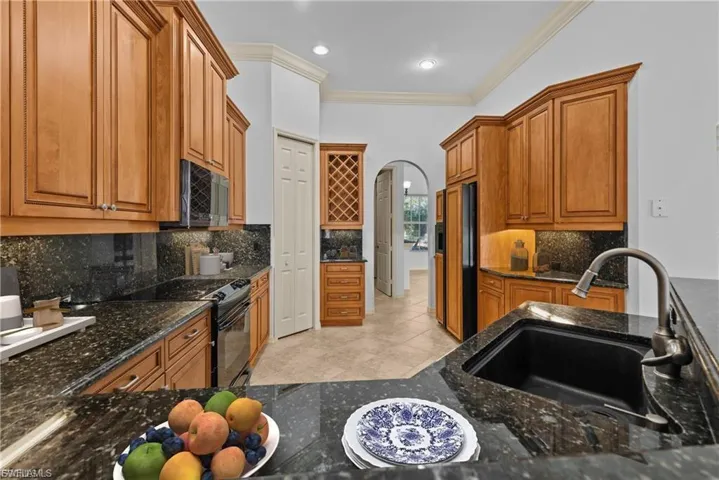 Kitchen featuring arched walkways, wood finish cabinetry, ornamental molding, dark stone countertops, and black electric range oven