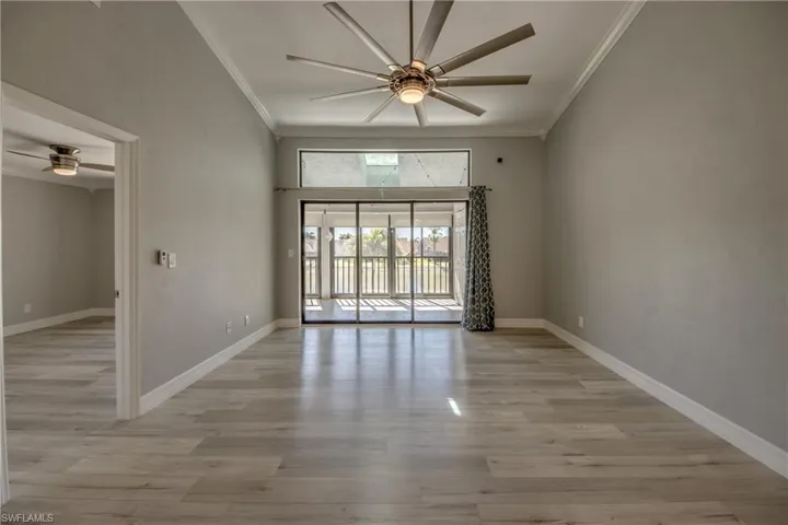 Spare room featuring a ceiling fan, light wood finished floors, ornamental molding, and a towering ceiling