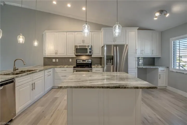 Kitchen featuring decorative backsplash, appliances with stainless steel finishes, lofted ceiling, white cabinetry, and hanging light fixtures