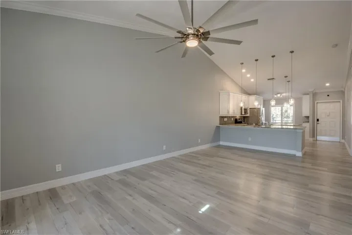 Unfurnished living room with ornamental molding, light wood-style floors, high vaulted ceiling, a chandelier, and a ceiling fan