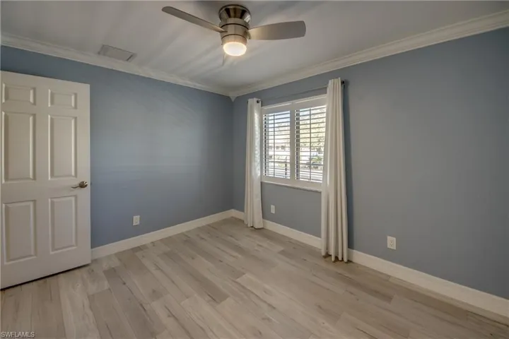 Empty room featuring ornamental molding, light wood-style floors, ceiling fan, and attic access