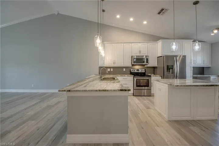 Kitchen featuring appliances with stainless steel finishes, vaulted ceiling, a peninsula, white cabinetry, and light stone counters