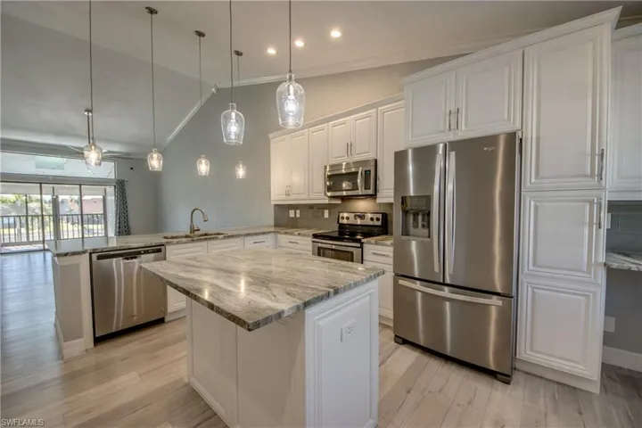 Kitchen with stainless steel appliances, white cabinetry, light stone counters, decorative light fixtures, and crown molding