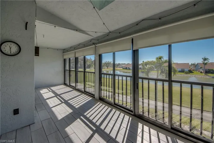 Unfurnished sunroom with a textured wall, a water view, wood tiled floors, a residential view, and vaulted ceiling