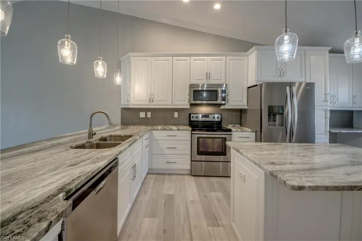 Kitchen featuring decorative light fixtures, lofted ceiling, appliances with stainless steel finishes, light stone countertops, and white cabinetry