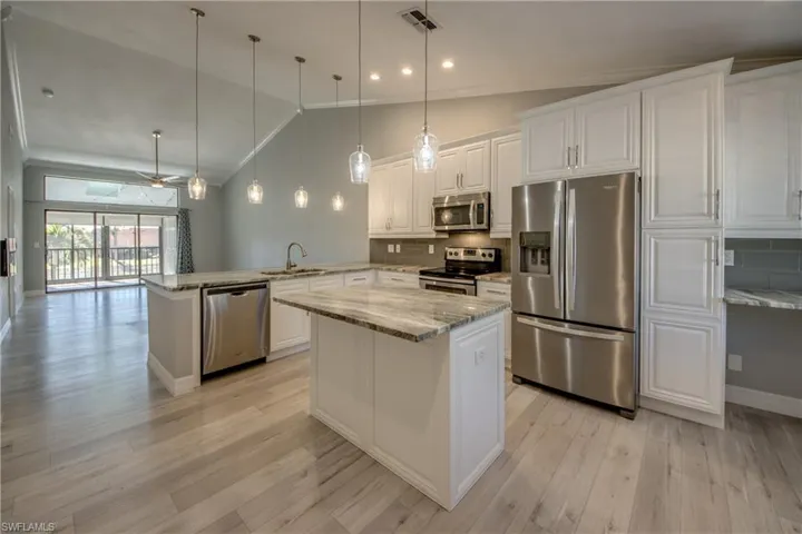 Kitchen with stainless steel appliances, white cabinetry, hanging light fixtures, light stone counters, and high vaulted ceiling