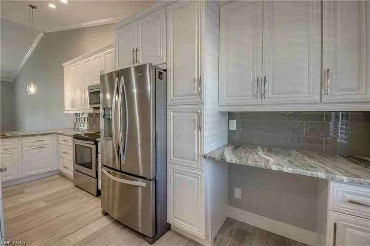 Kitchen featuring stainless steel appliances, pendant lighting, white cabinetry, vaulted ceiling, and light stone countertops