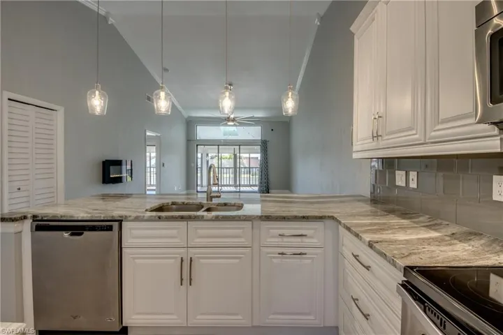 Kitchen with stainless steel appliances, open floor plan, ceiling fan, decorative light fixtures, and ornamental molding