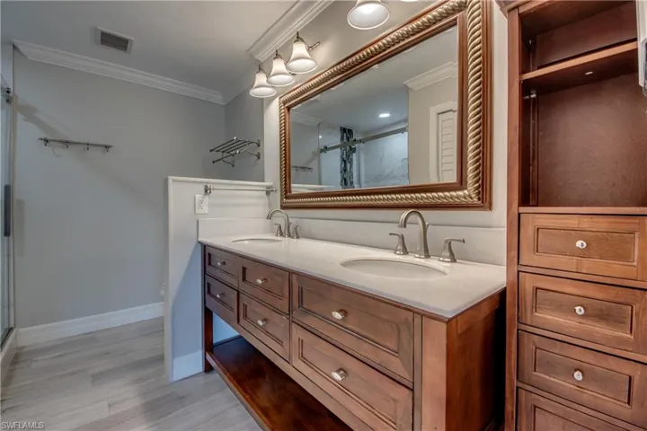 Bathroom with a stall shower, ornamental molding, double vanity, and light wood-type flooring