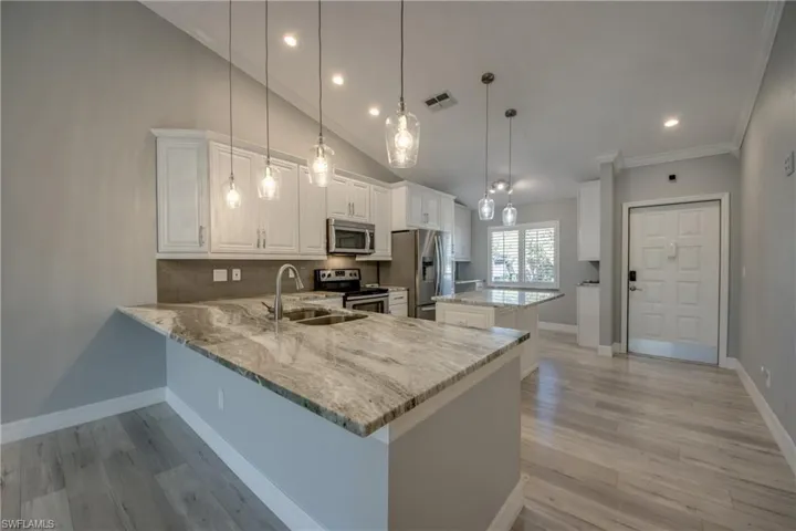 Kitchen featuring a kitchen island, recessed lighting, a peninsula, white cabinetry, and light stone counters