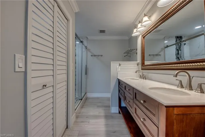 Full bathroom with a closet, crown molding, a stall shower, double vanity, and light wood finished floors