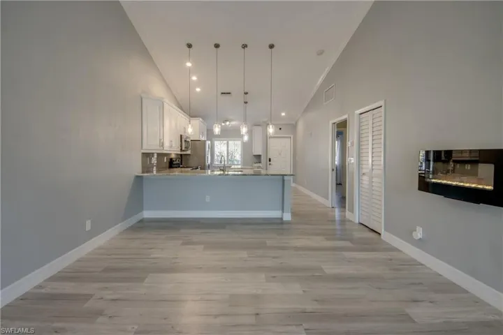 Kitchen with white cabinetry, a peninsula, crown molding, decorative light fixtures, and high vaulted ceiling