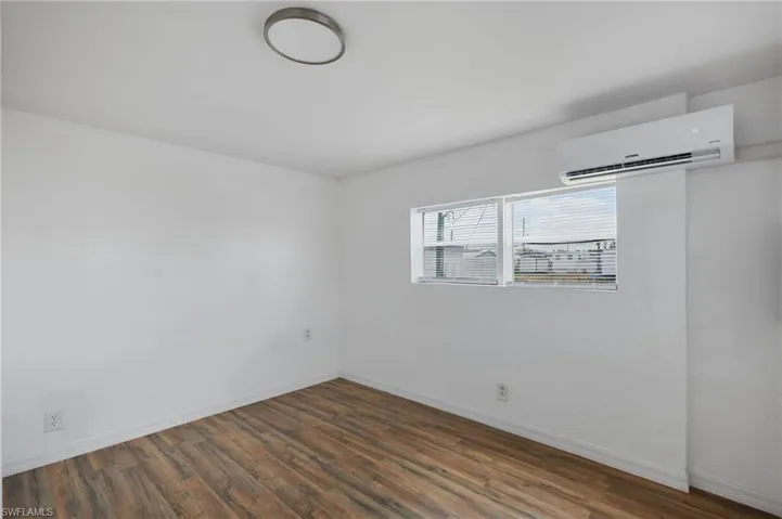 Empty room with baseboards, a wall mounted AC, and wood finished floors