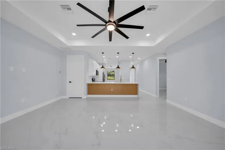 Spacious room featuring tray ceilings with a contemporary ceiling fan, recessed lighting, and glossy light-toned flooring