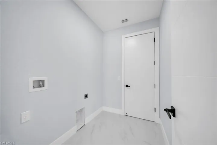 Dedicated utility area featuring connections for laundry appliances, light gray wall paint, white baseboards, and a white door with a black handle