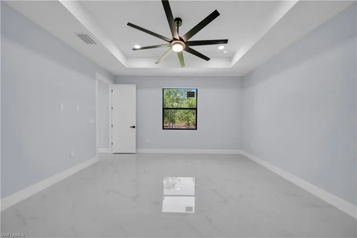 Recessed tray ceiling with a modern ceiling fan, light gray walls, and large format tile flooring