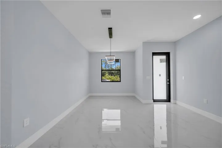 Spacious room featuring light-toned walls, contemporary lighting fixtures, and large format tile flooring
