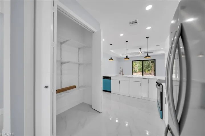 Kitchen pantry with adjustable shelving, showcasing a modern open-concept kitchen with white cabinetry, light countertops, and recessed lighting