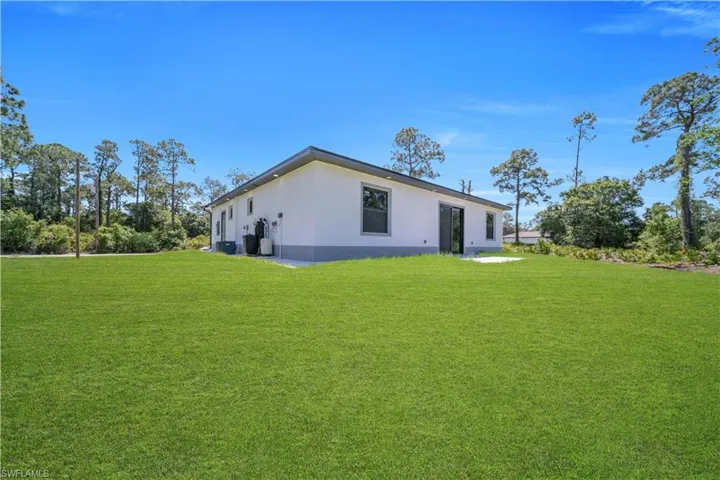 Expansive green lawn surrounds the residence, featuring a white stucco exterior with gray trim
