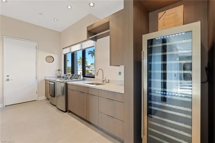 Kitchen featuring beverage cooler, washer and clothes dryer, recessed lighting, modern cabinets, and light tile patterned flooring