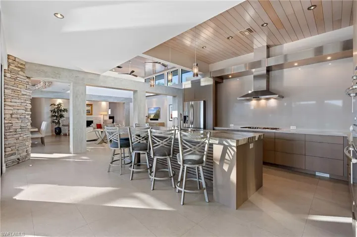 Kitchen with modern cabinets, a breakfast bar, a towering ceiling, light tile patterned floors, and wall chimney exhaust hood