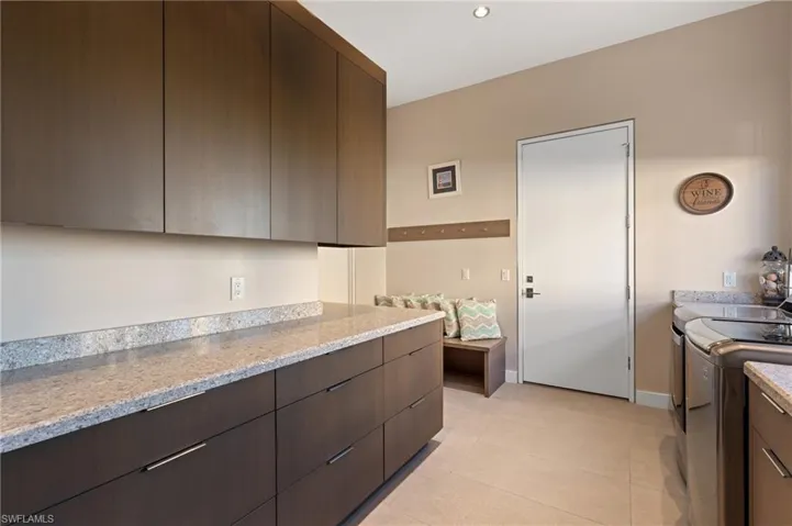 Kitchen featuring modern cabinets, washing machine and clothes dryer, dark brown cabinetry, light tile patterned floors, and light stone counters