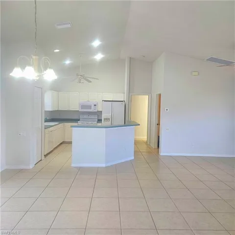 Kitchen with ceiling fan, dark countertops, vaulted ceiling, white appliances, and suspended lighting