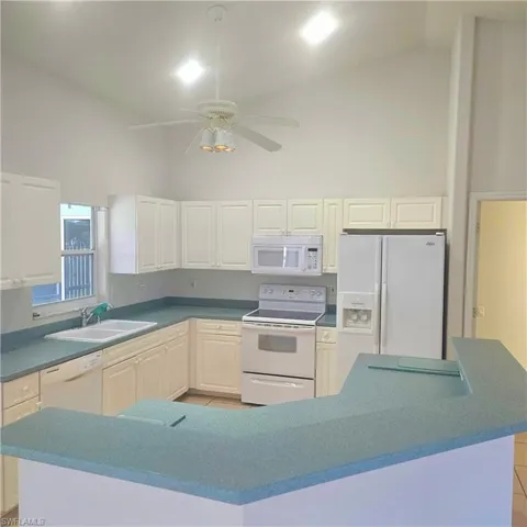 Kitchen with white appliances, a ceiling fan, lofted ceiling, dark countertops, and white cabinetry