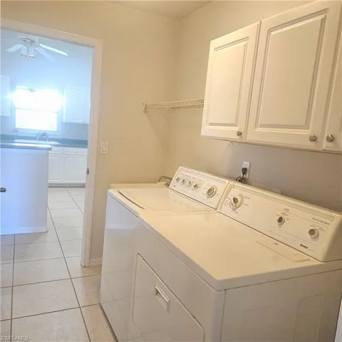 Laundry room with a ceiling fan, light tile patterned floors, washer and dryer, and cabinet space
