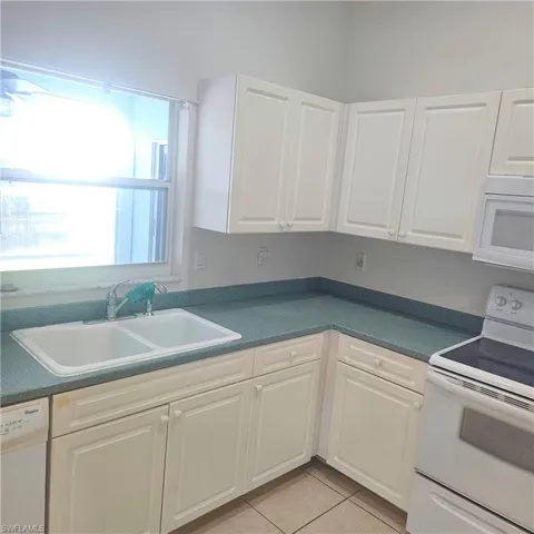 Kitchen featuring white appliances, white cabinetry, dark countertops, and light tile patterned floors