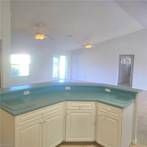 Kitchen with open floor plan, ceiling fan, dark countertops, light tile patterned floors, and lofted ceiling