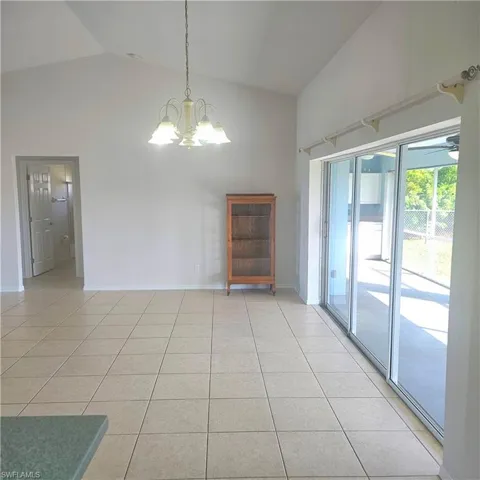 Unfurnished dining area featuring a chandelier, lofted ceiling, light tile patterned floors, and a ceiling fan