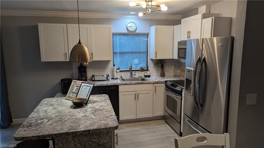 Kitchen with backsplash, stainless steel appliances, a notable chandelier, sink, and ornamental molding