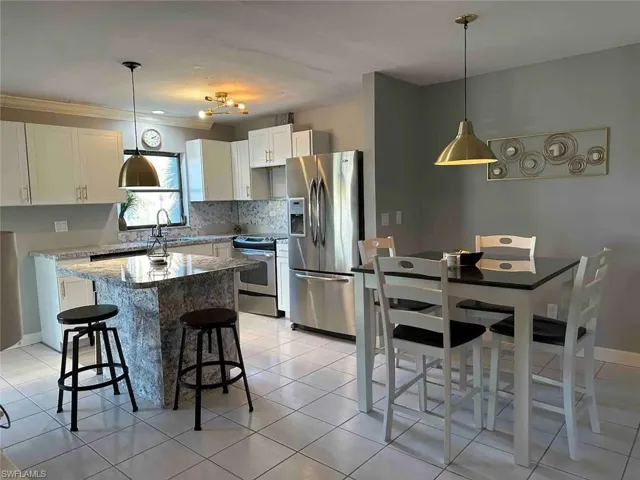 Kitchen with appliances with stainless steel finishes, white cabinetry, light stone counters, and hanging light fixtures